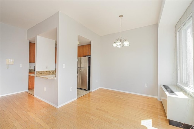 kitchen with freestanding refrigerator, brown cabinets, a chandelier, light wood finished floors, and baseboards
