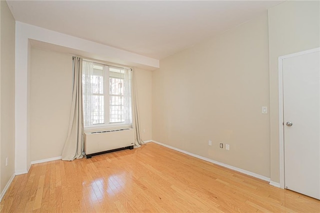 empty room featuring hardwood / wood-style floors, baseboards, and radiator heating unit