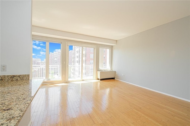 unfurnished room featuring light wood-style flooring, baseboards, a city view, and radiator heating unit