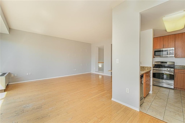 kitchen with stainless steel appliances, brown cabinets, light wood finished floors, and baseboards