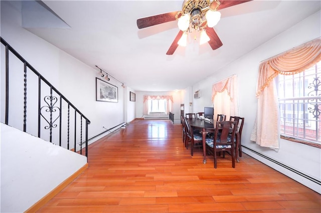 dining area with a baseboard radiator, light wood-type flooring, stairway, and a ceiling fan