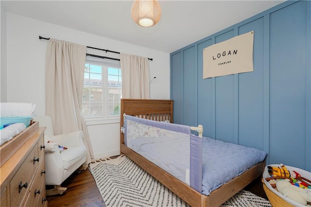 bedroom featuring a decorative wall and dark wood-style floors