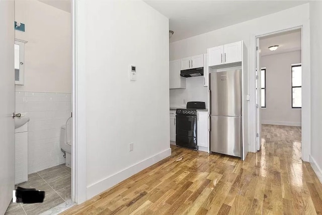 121 Lewis Ave, Brooklyn, NY 11221 - kitchen featuring black stove, light wood-style flooring, under cabinet range hood, white cabinetry, and freestanding refrigerator