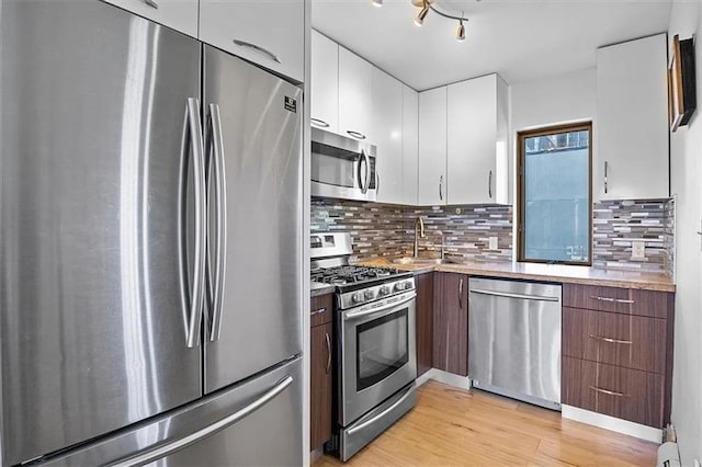kitchen with appliances with stainless steel finishes, a sink, white cabinetry, light wood finished floors, and tasteful backsplash