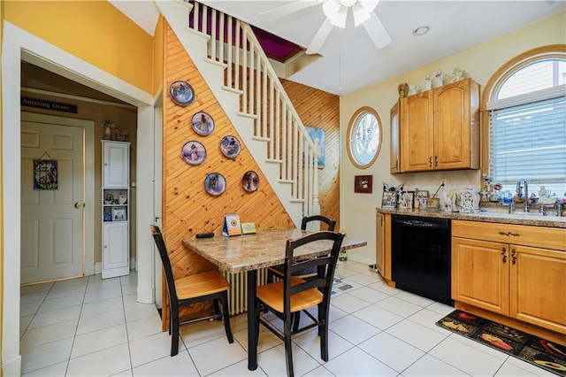 kitchen featuring dishwasher, a sink, ceiling fan, light tile patterned flooring, and wooden walls