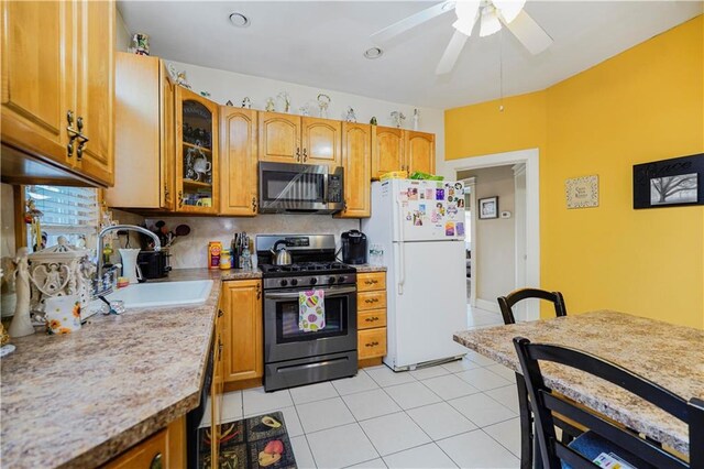 kitchen with appliances with stainless steel finishes, a sink, ceiling fan, glass insert cabinets, and brown cabinets