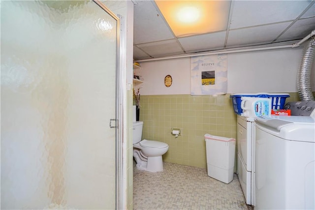 full bathroom featuring washer and clothes dryer, tile patterned floors, a stall shower, toilet, and tile walls