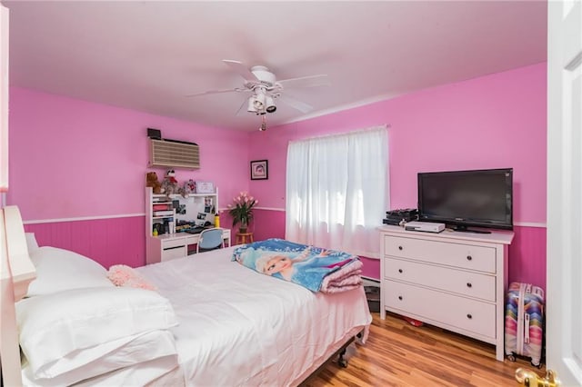 bedroom featuring light wood-type flooring, ceiling fan, and a wall mounted AC