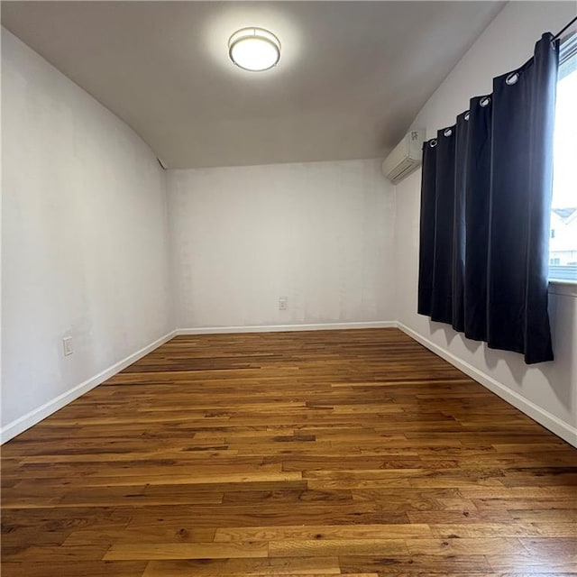 spare room with an AC wall unit, baseboards, vaulted ceiling, and hardwood / wood-style floors