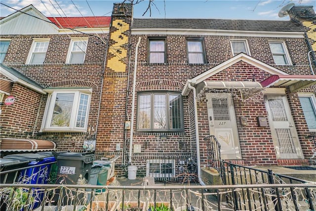 townhome / multi-family property featuring a chimney, brick siding, and fence