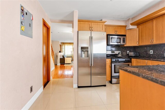 kitchen featuring tasteful backsplash, light tile patterned floors, dark stone countertops, baseboards, and appliances with stainless steel finishes