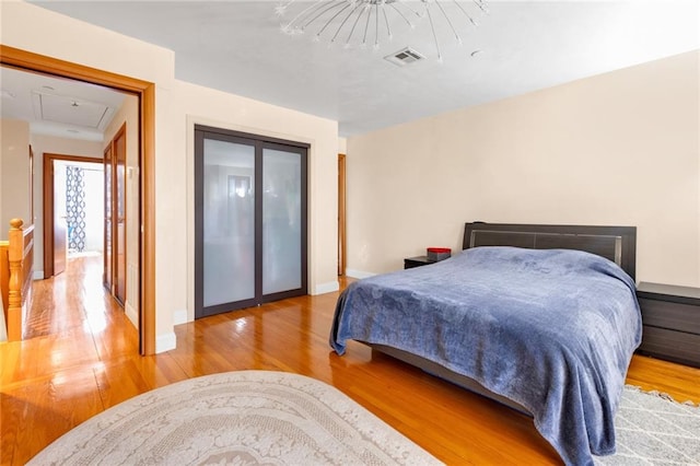bedroom with baseboards, visible vents, wood finished floors, and attic access
