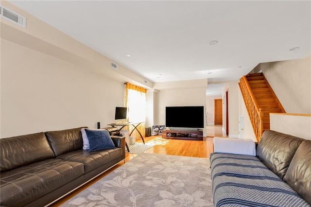 living room with stairs, visible vents, and wood finished floors