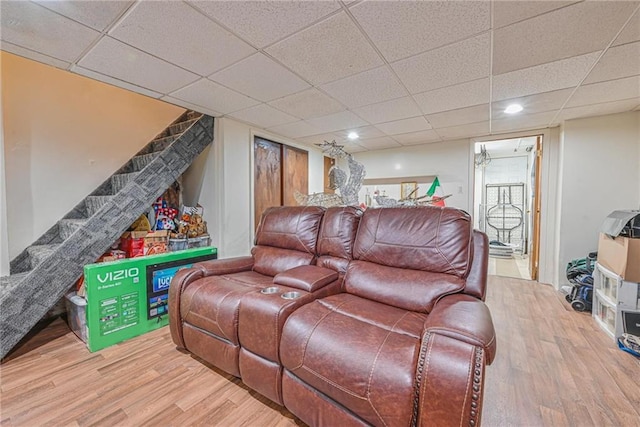 living area featuring wood finished floors, a drop ceiling, and stairway
