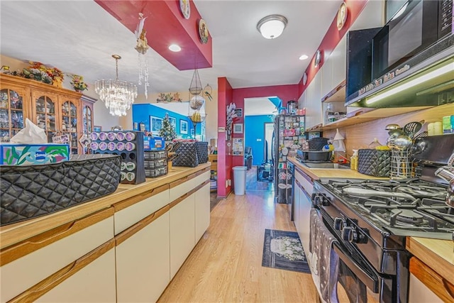 kitchen with butcher block countertops, light wood finished floors, a chandelier, and gas range oven
