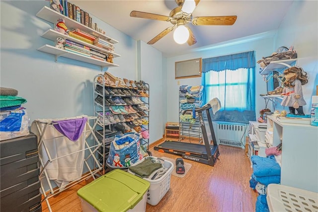 exercise area with ceiling fan, radiator, and wood finished floors