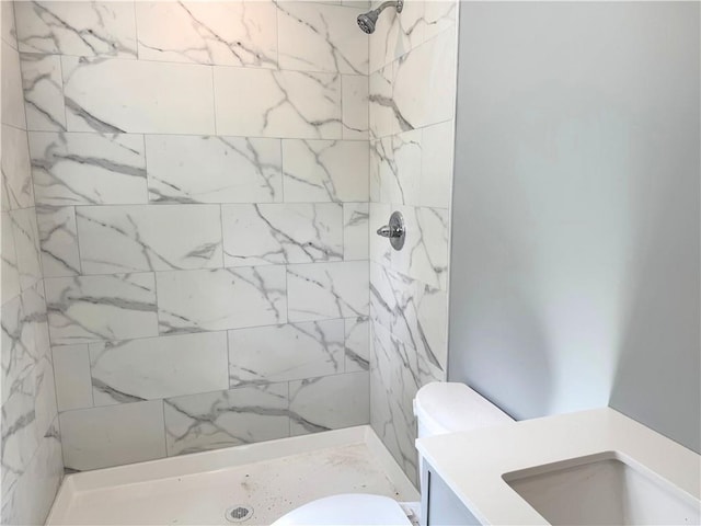 full bathroom featuring toilet, a tile shower, and vanity