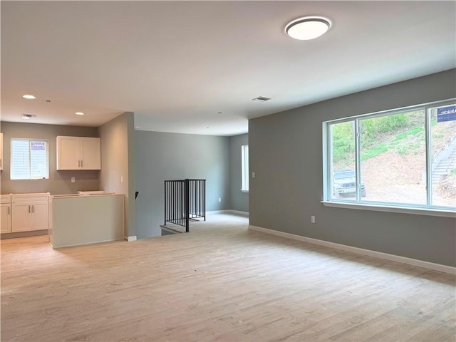 unfurnished living room with baseboards, a wealth of natural light, and light wood finished floors