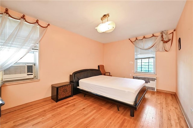 bedroom featuring radiator heating unit, cooling unit, light wood-type flooring, and baseboards
