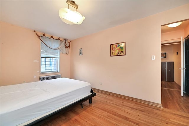 bedroom featuring light wood-style flooring, baseboards, and radiator