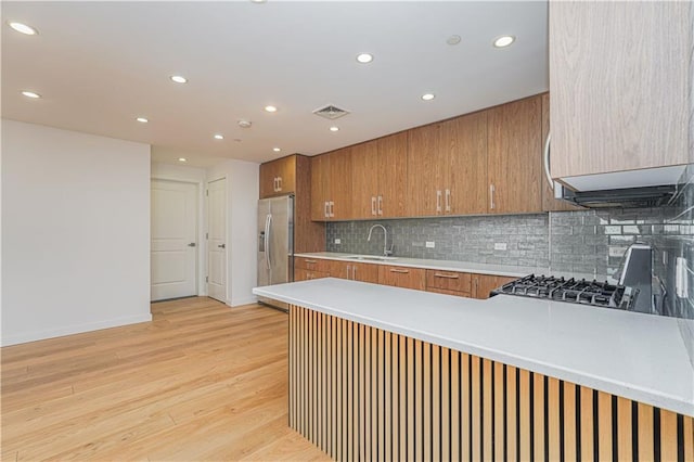 kitchen featuring a sink, stainless steel fridge with ice dispenser, brown cabinetry, recessed lighting, and a peninsula