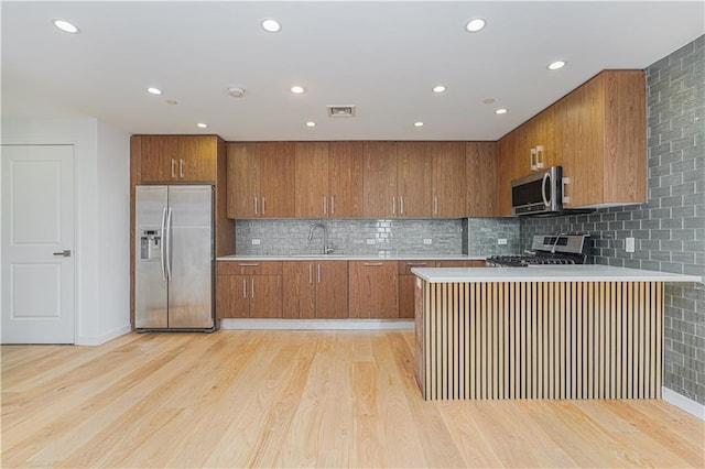 kitchen with appliances with stainless steel finishes, brown cabinets, light countertops, light wood-style flooring, and recessed lighting