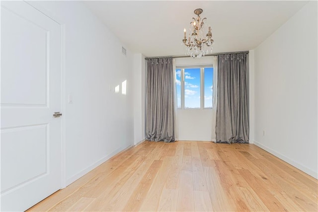 empty room with wood finished floors, a chandelier, and baseboards