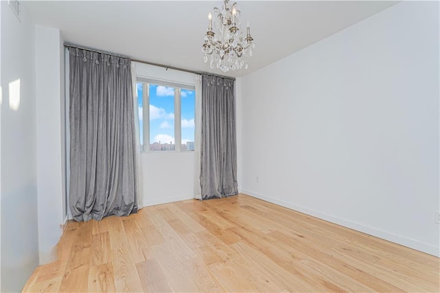 spare room featuring a chandelier, wood finished floors, and baseboards