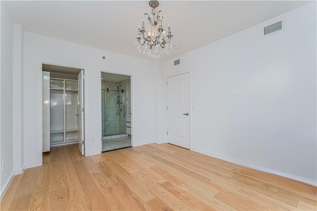unfurnished bedroom with a chandelier, a spacious closet, light wood-style flooring, and a closet
