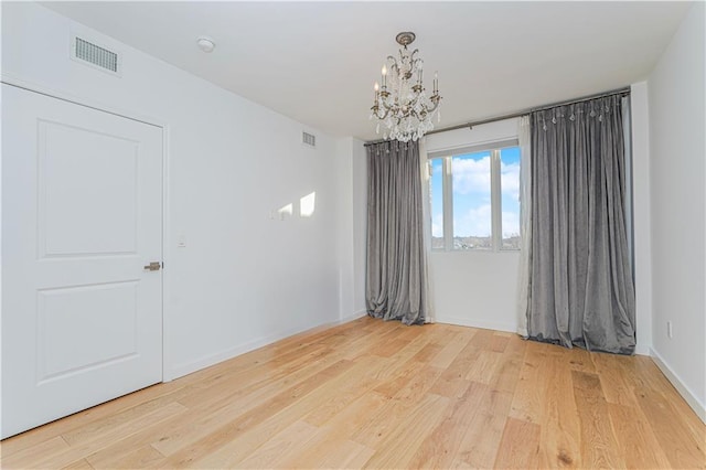 spare room with a chandelier, light wood-type flooring, and baseboards