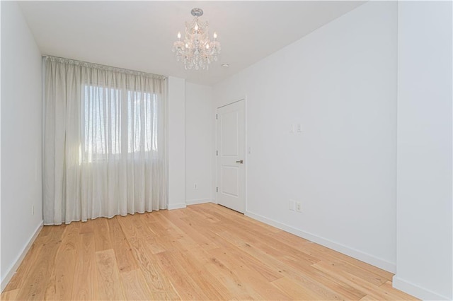 empty room with a chandelier, baseboards, and wood finished floors