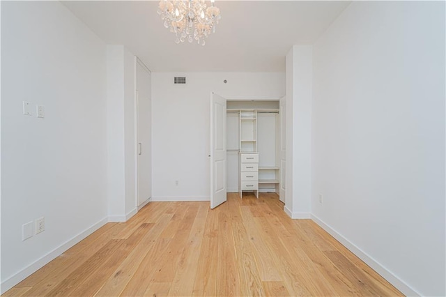 unfurnished bedroom featuring light wood-style flooring, a chandelier, baseboards, and a closet