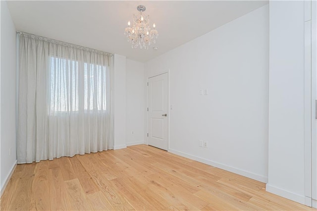 unfurnished room featuring a chandelier, light wood-style flooring, and baseboards