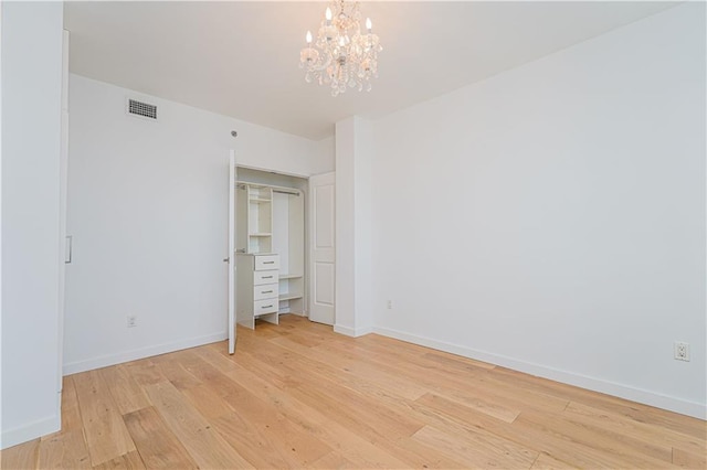 unfurnished bedroom with light wood-type flooring, a chandelier, and baseboards