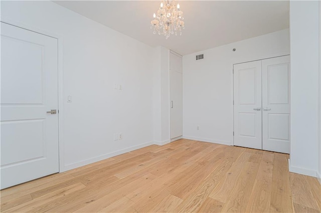 unfurnished bedroom featuring light wood-style floors, a chandelier, baseboards, and a closet