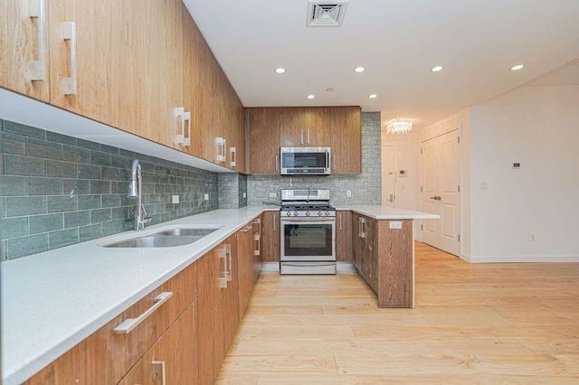kitchen featuring stainless steel appliances, a sink, light wood-style floors, recessed lighting, and backsplash