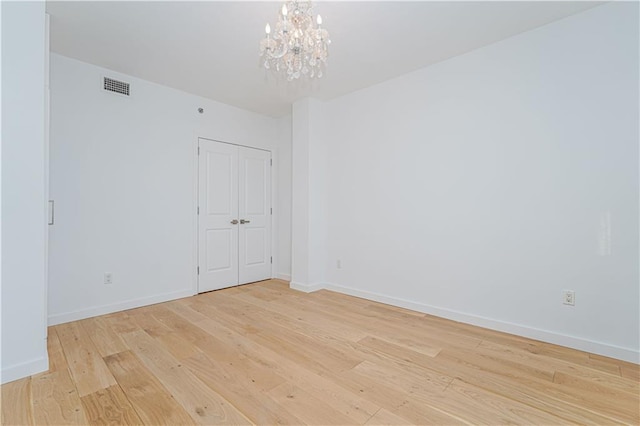 unfurnished room featuring light wood-type flooring, a chandelier, and baseboards