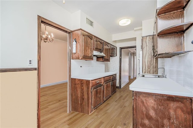 kitchen with a sink, visible vents, light wood-style floors, light countertops, and under cabinet range hood