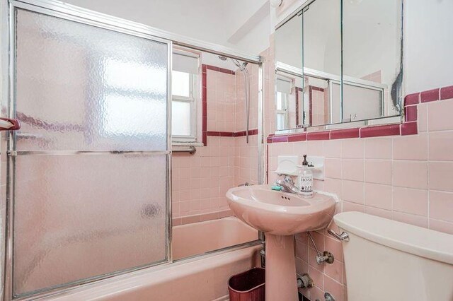 bathroom featuring decorative backsplash, a sink, enclosed tub / shower combo, toilet, and tile walls