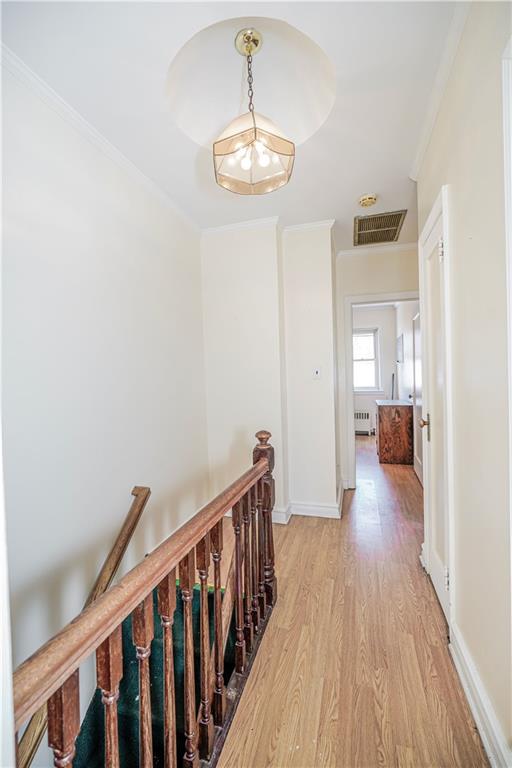 hallway featuring an upstairs landing, light wood-style floors, visible vents, ornamental molding, and radiator heating unit