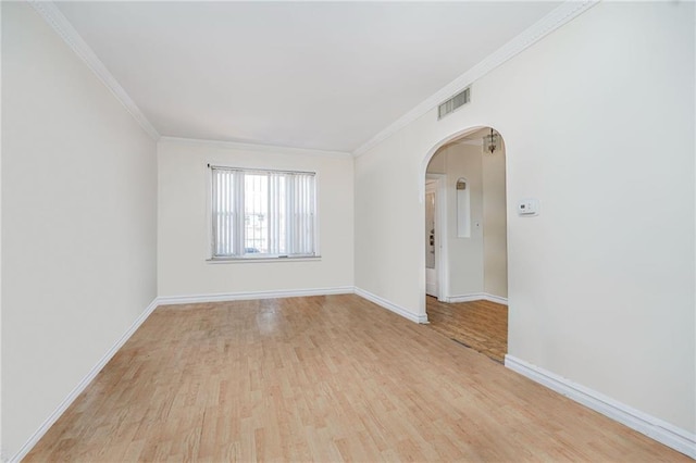 empty room with arched walkways, ornamental molding, light wood finished floors, baseboards, and visible vents