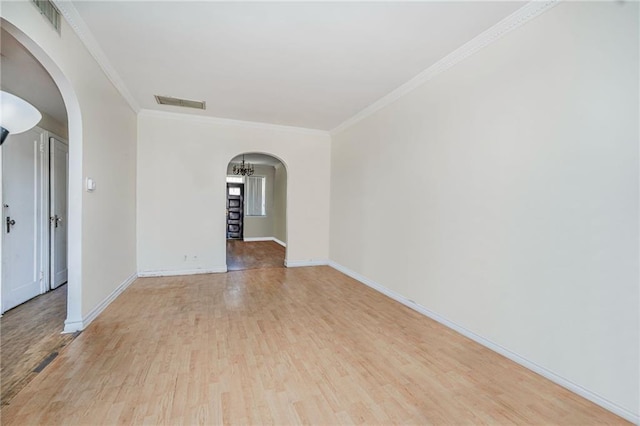 spare room featuring wood finished floors, visible vents, ornamental molding, and arched walkways