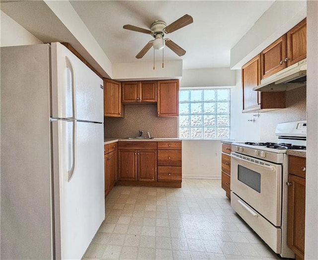 kitchen with brown cabinetry, a sink, white appliances, under cabinet range hood, and a ceiling fan