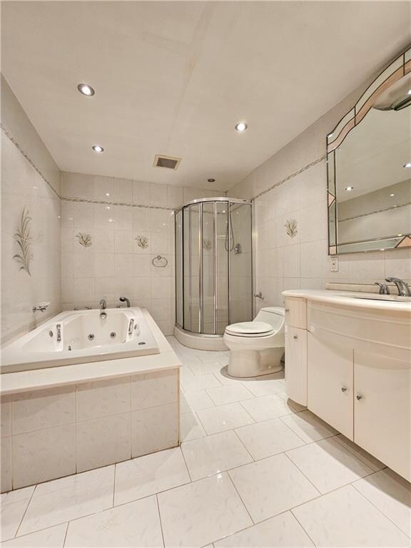 bathroom with visible vents, vanity, tile walls, a whirlpool tub, and a stall shower
