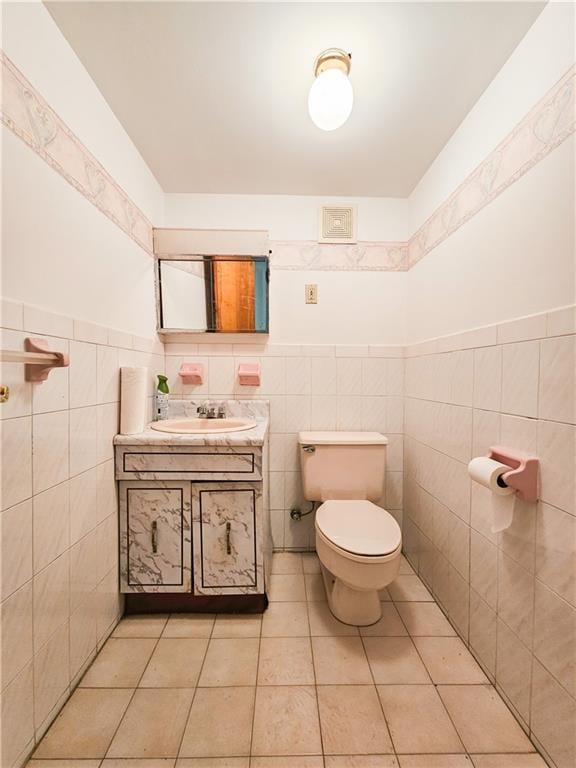 half bathroom featuring tile walls, tile patterned flooring, wainscoting, vanity, and toilet