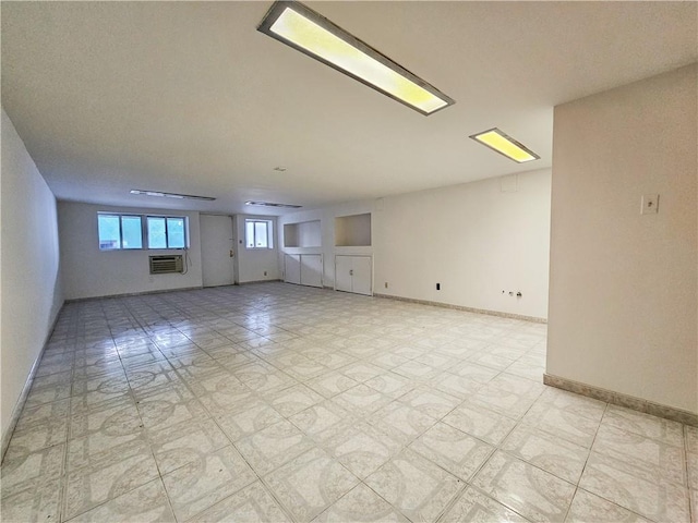 spare room with baseboards, an AC wall unit, and light floors