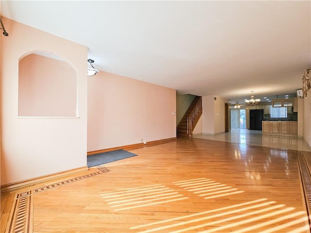 unfurnished living room featuring light wood-style floors, baseboards, stairway, and an inviting chandelier