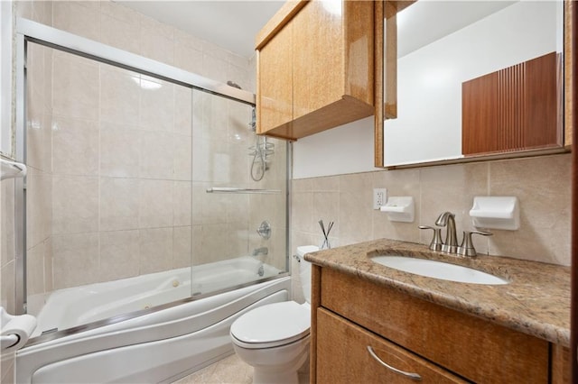bathroom with tile walls, bath / shower combo with glass door, toilet, and vanity