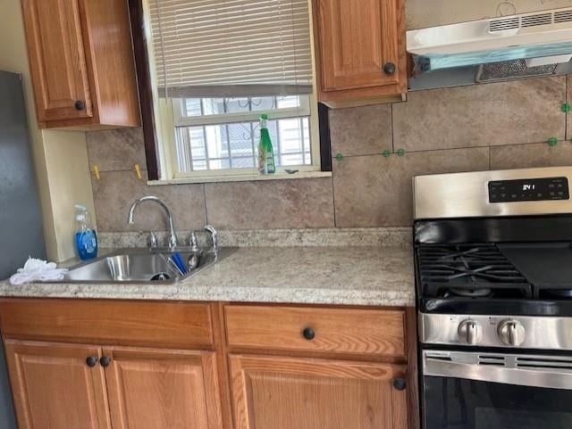 kitchen featuring light countertops, tasteful backsplash, under cabinet range hood, gas stove, and a sink
