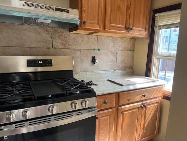 kitchen featuring brown cabinetry, stainless steel gas range, tasteful backsplash, and under cabinet range hood